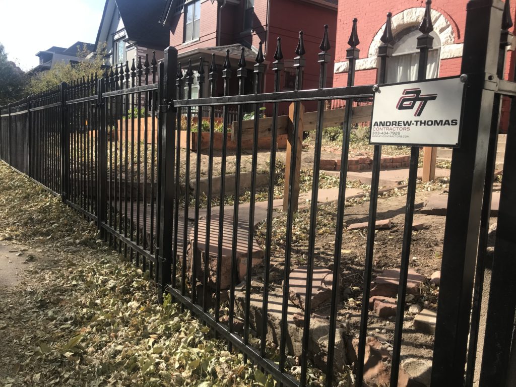 Wrought iron fence with Andrew Thomas logo enclosing a house