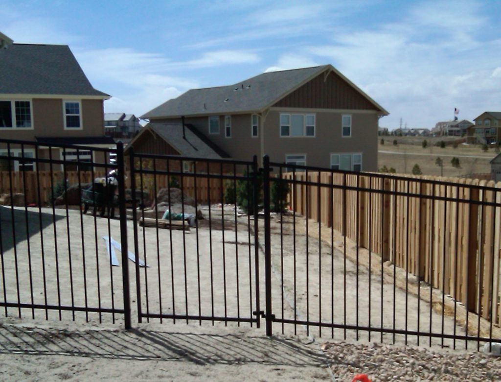 a cemented backyard enclosed in wrought iron fence and wooden fence in Denver, Colorado