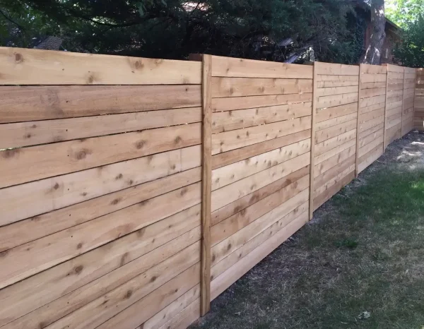 Long wooden privacy fence with horizontal planks and vertical posts along a grassy yard.