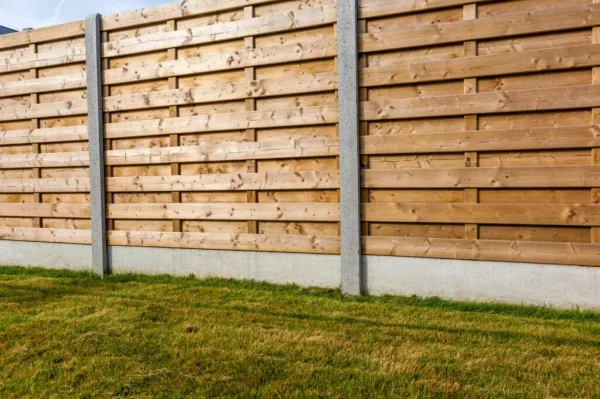 Wooden fence with horizontal planks and concrete posts, set on a grassy lawn.
